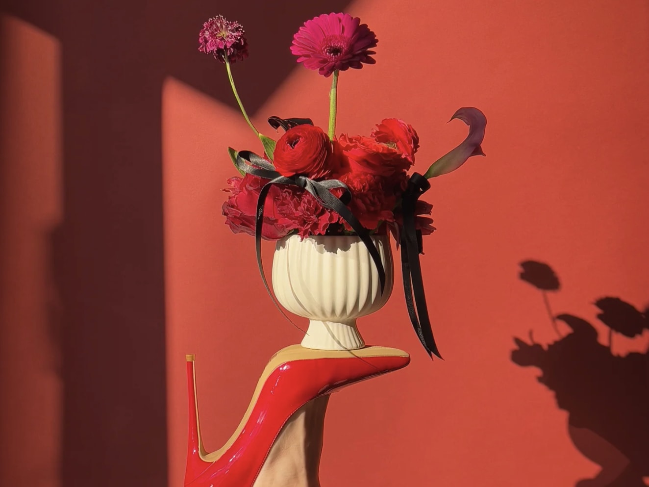 A red high-heeled shoe supports a white vase filled with vibrant red and pink flowers in Atlanta, Georgia.